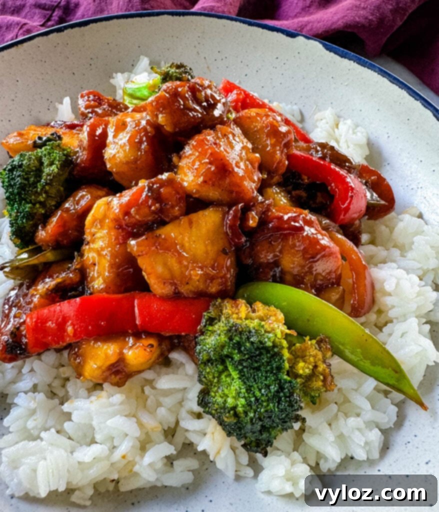 Orange chicken with stir-fried vegetables and white rice elegantly plated in a white bowl.