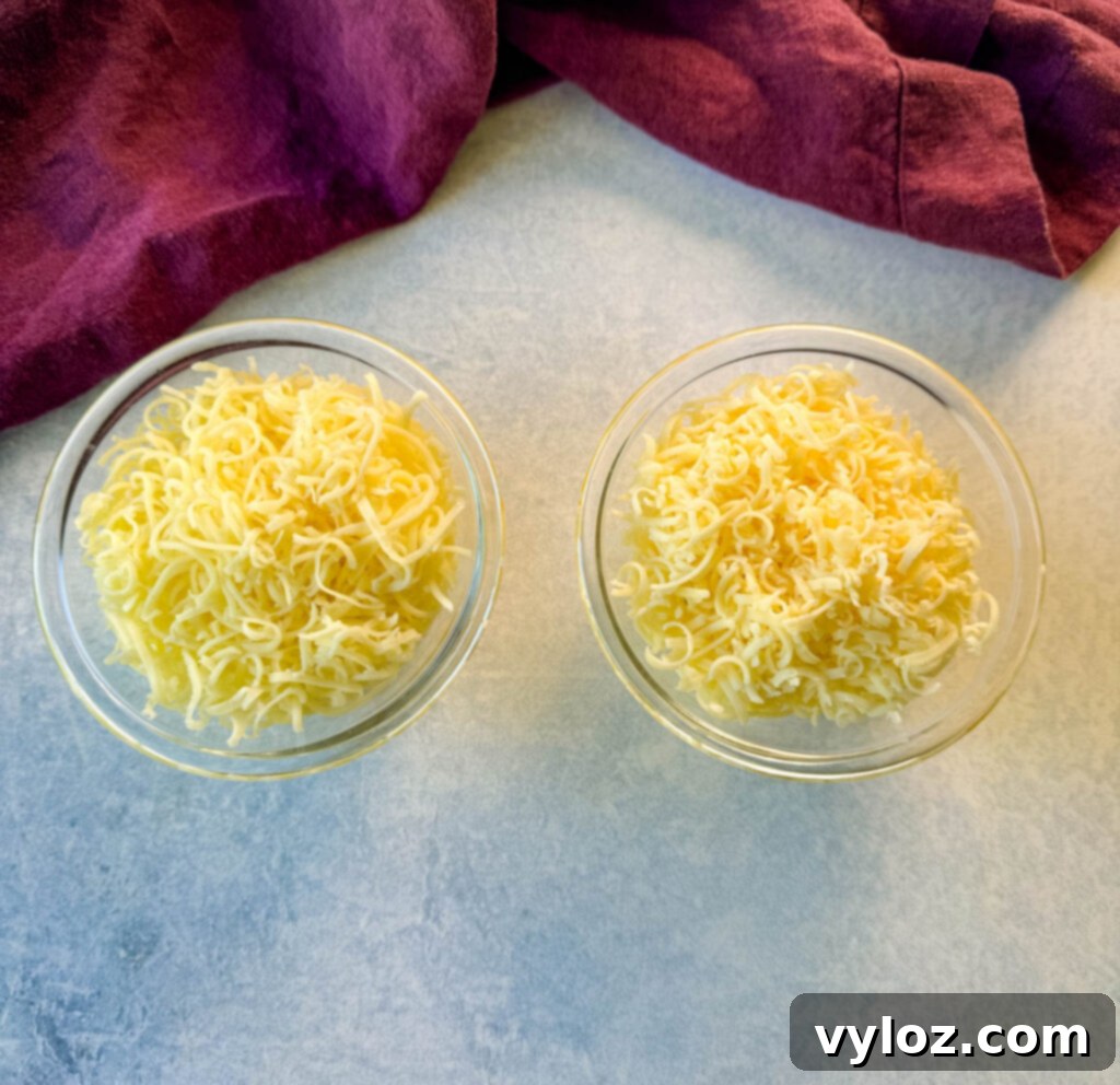 Close-up of freshly grated white cheddar cheese in glass bowls, illustrating cheese options for homemade Cheez Whiz