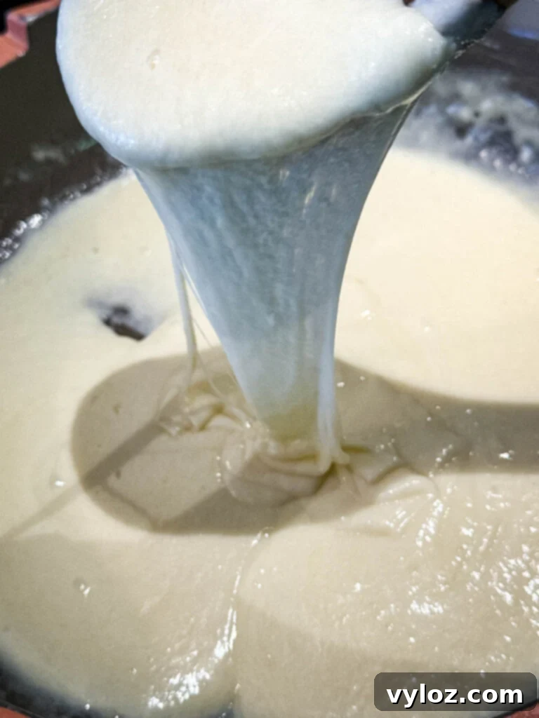 A glorious cheese pull of homemade Cheez Whiz being lifted from a skillet, showing its elasticity