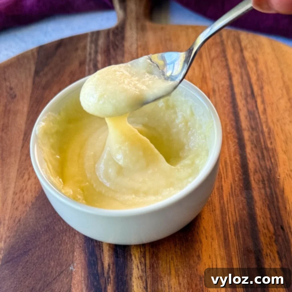 A spoonful of homemade Cheez Whiz being lifted from a white bowl, showing its thick and smooth consistency