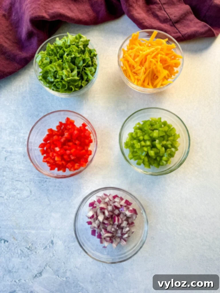 lettuce, grated cheddar cheese, diced red peppers, diced green peppers, and diced onions in separate glass bowls
