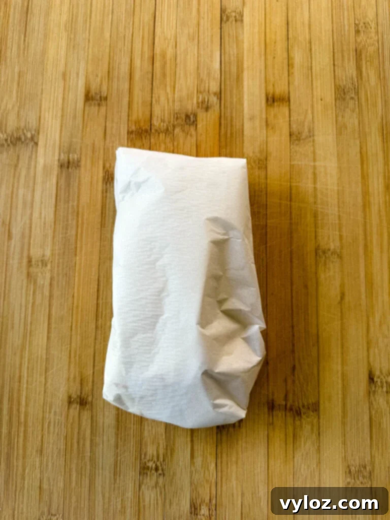 breakfast burritos wrapped with parchment paper with bacon, potatoes, bell peppers and cheese on a flat surface