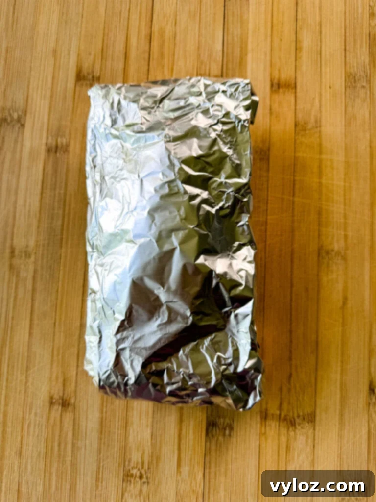 breakfast burritos wrapped with parchment paper and foil with bacon, potatoes, bell peppers and cheese on a flat surface