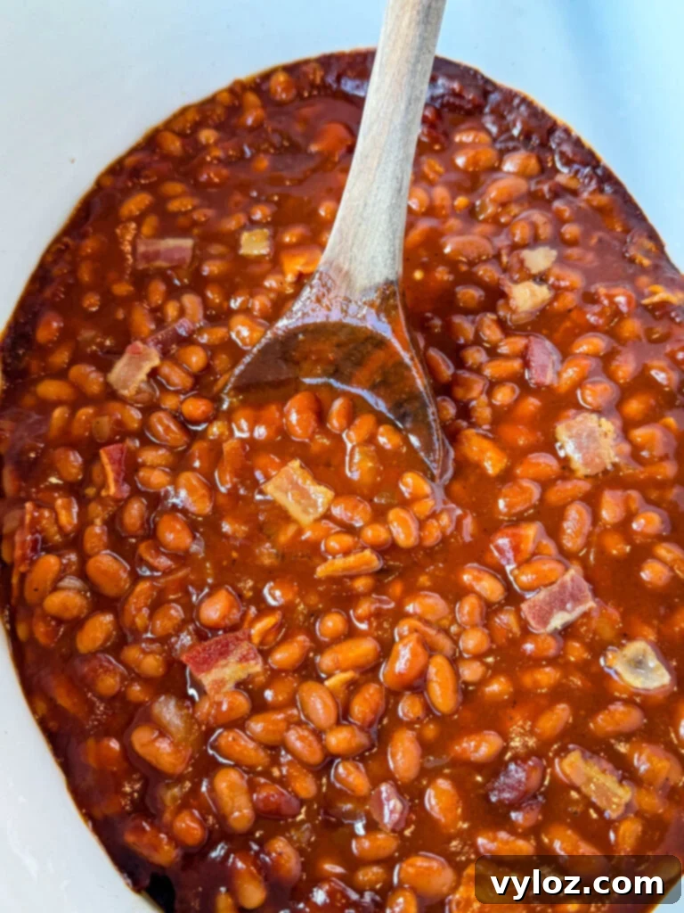 Smoky Slow Cooker Bacon Baked Beans 2 baked beans in a slow cooker Crockpot with a wooden spoon