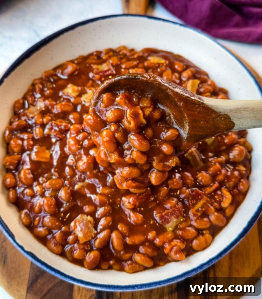 Smoky Slow Cooker Bacon Baked Beans 11 slow cooker Crockpot baked beans in a white bowl with a wooden spoon