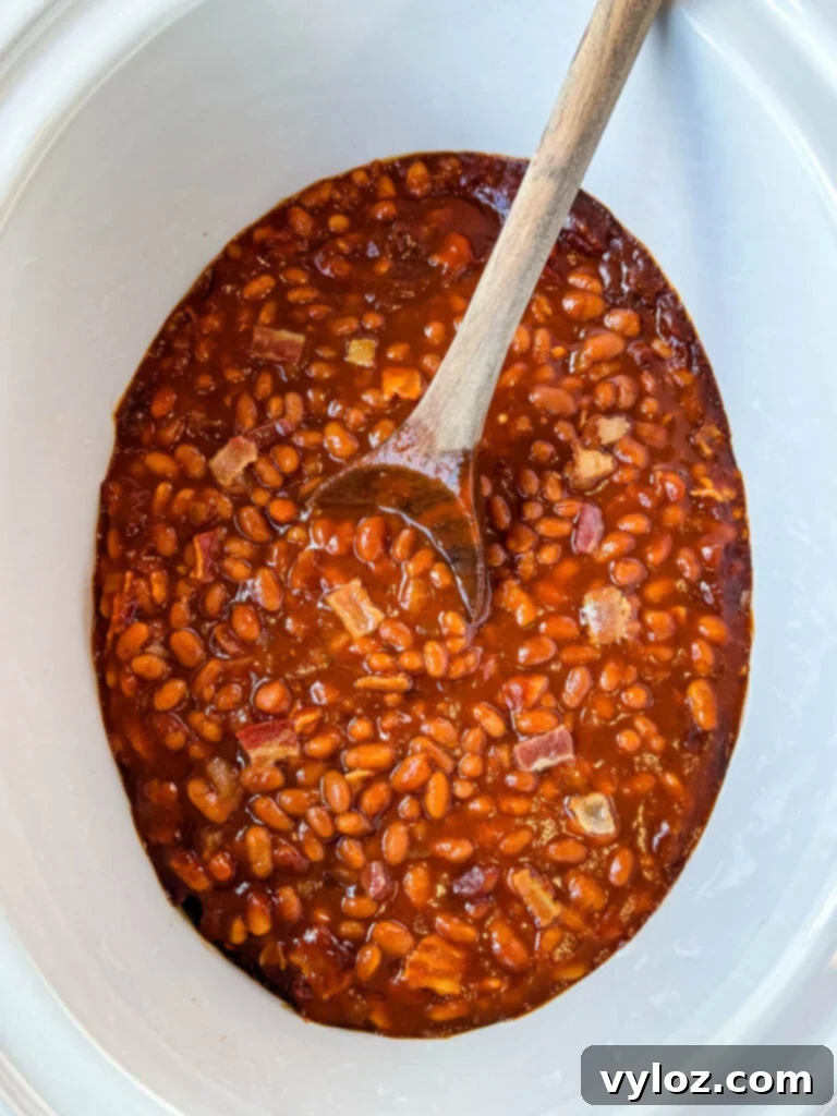 Smoky Slow Cooker Bacon Baked Beans 8 baked beans in a slow cooker Crockpot with a wooden spoon