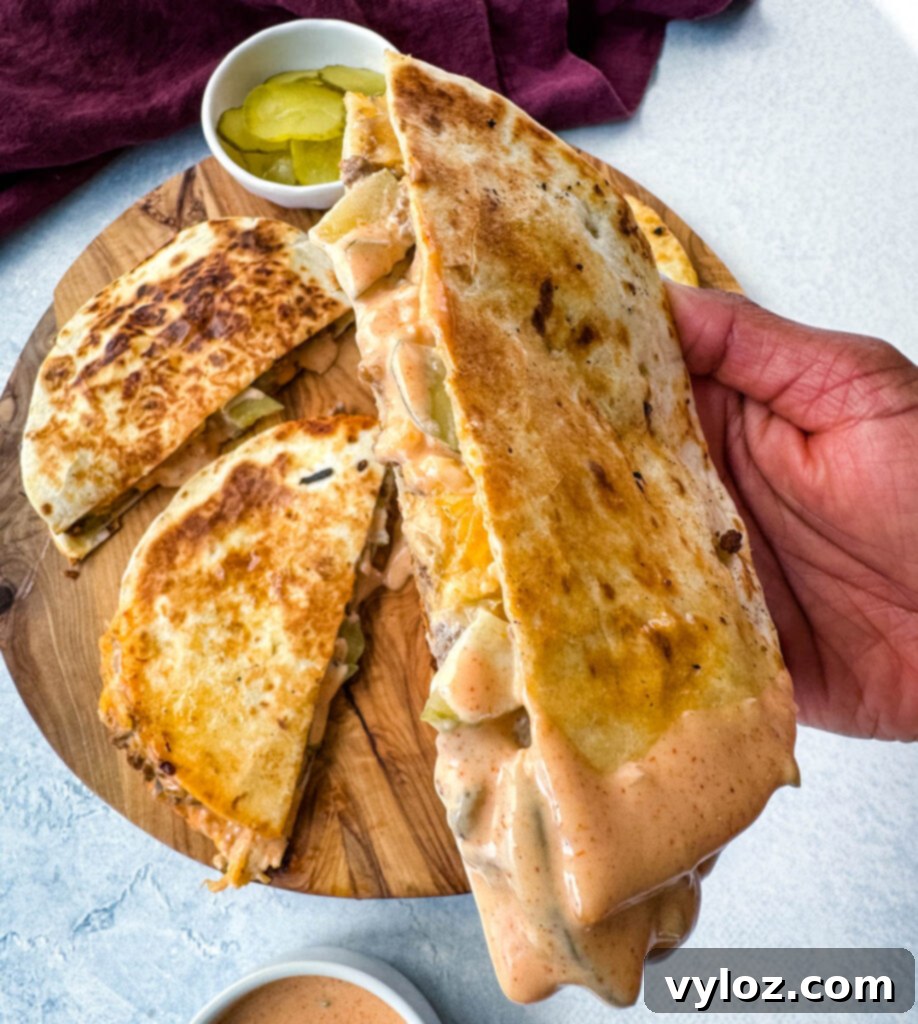 person holding cheeseburger quesadilla with pickles and burger sauce