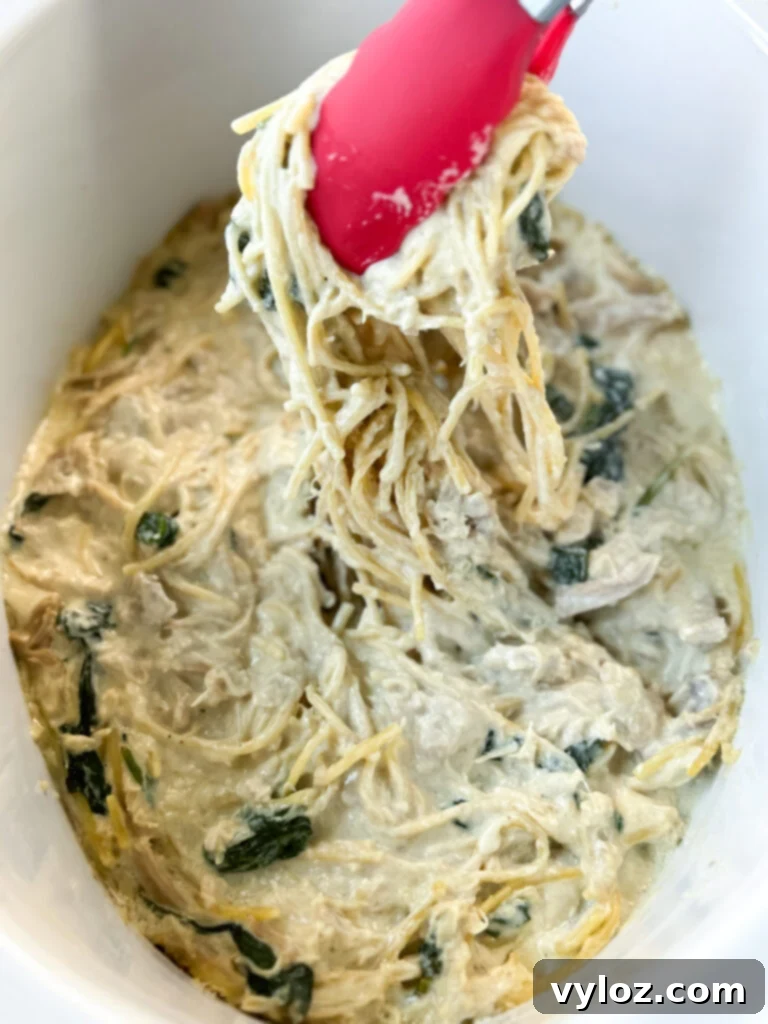 tongs filled with chicken alfredo in a Crockpot slow cooker