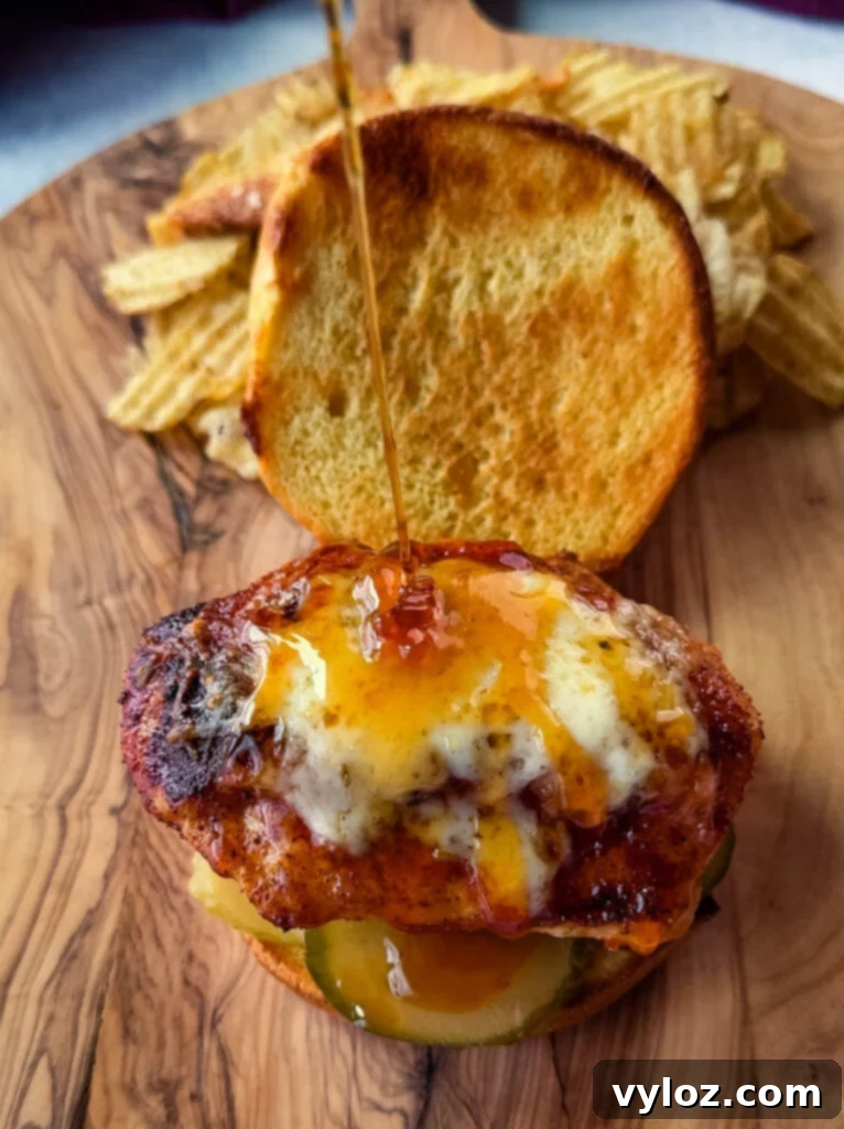 Hot honey sauce drizzled over a hot honey chicken sandwich with a brioche bun, pickles, and pepper jack cheese on a plate with chips