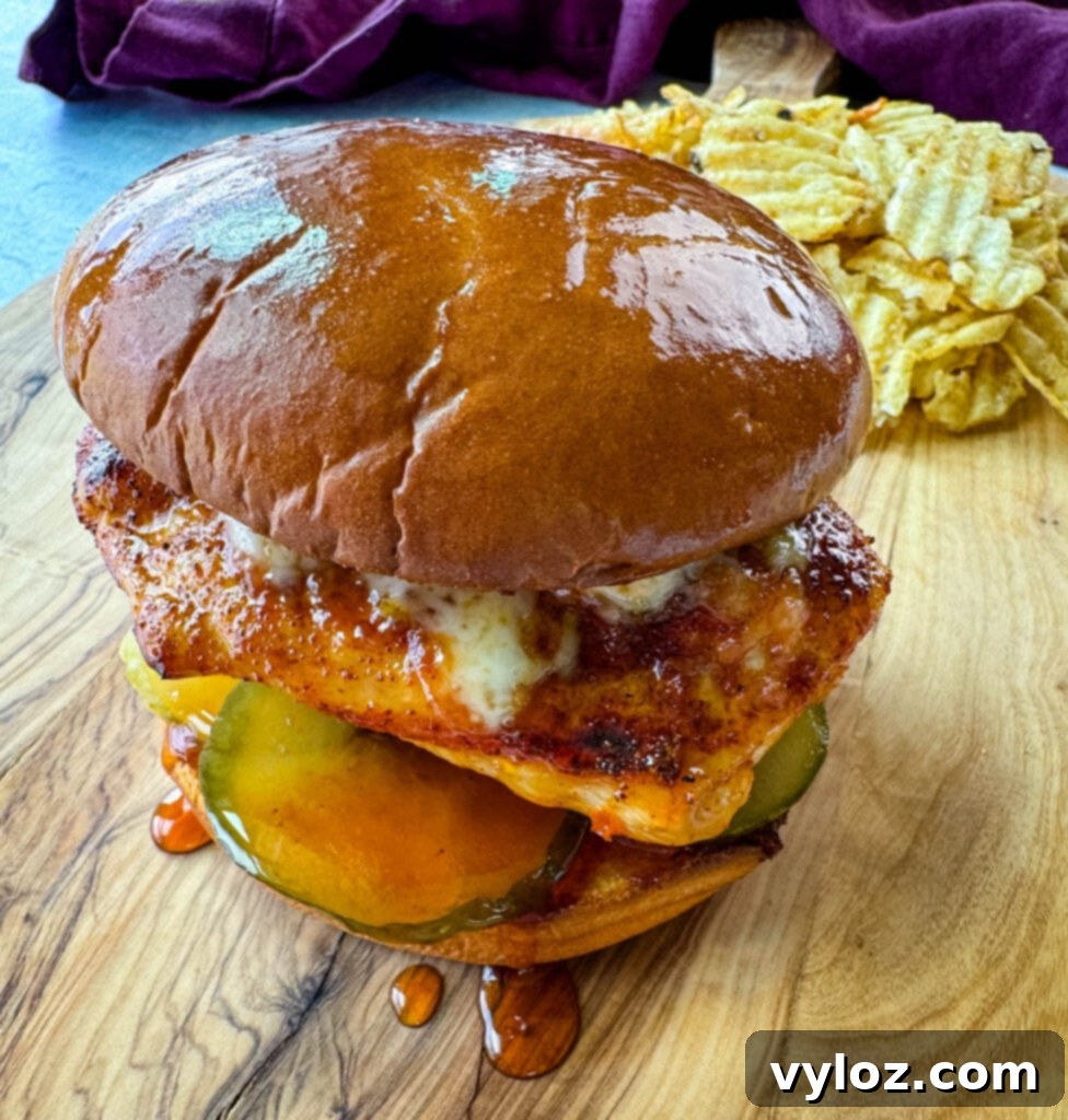 Hot honey chicken sandwich with a brioche bun, pickles, and pepperjack cheese on a plate with chips