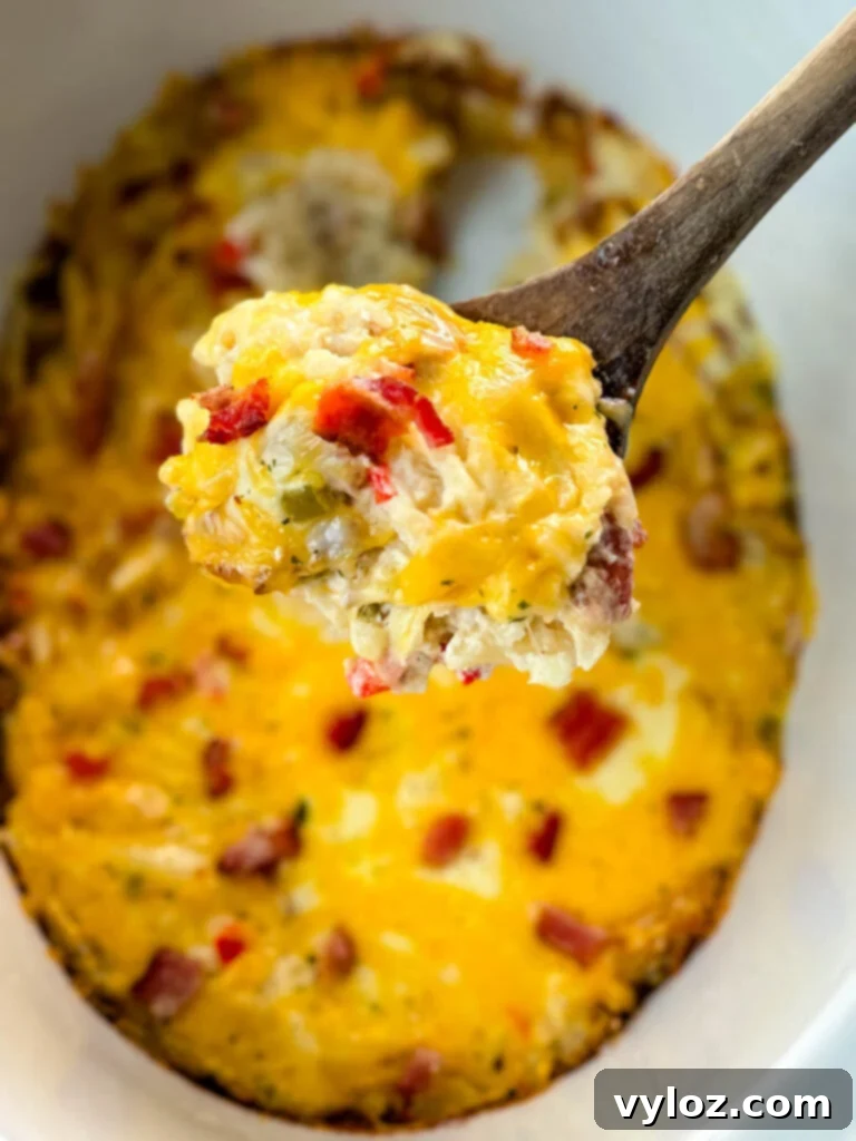 A wooden spoon lifting a serving of cheesy hash brown casserole from a Crockpot slow cooker, showcasing melted cheese and golden potatoes.