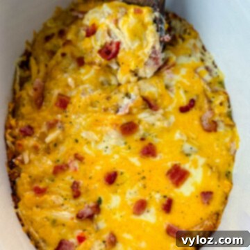 A wooden spoonful of hash brown casserole with melted cheese in a Crockpot slow cooker, ready for serving.