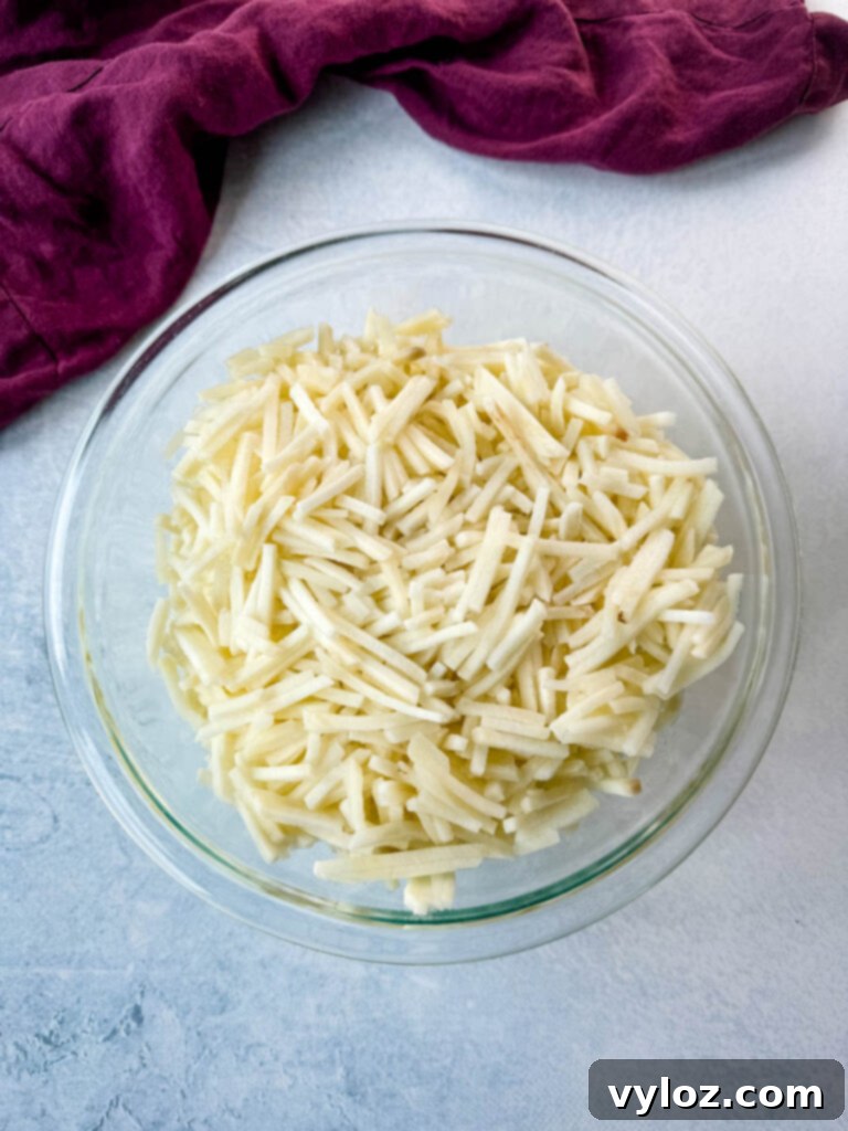A clear glass bowl filled with thawed, shredded hash browns, ready for use in a casserole.
