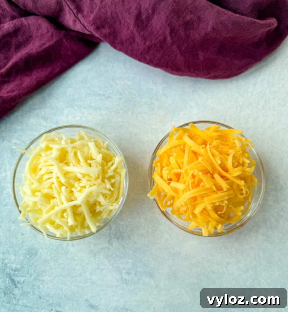 Two glass bowls side-by-side, one filled with shredded cheddar cheese and the other with shredded mozzarella cheese, ready to be added to the casserole.