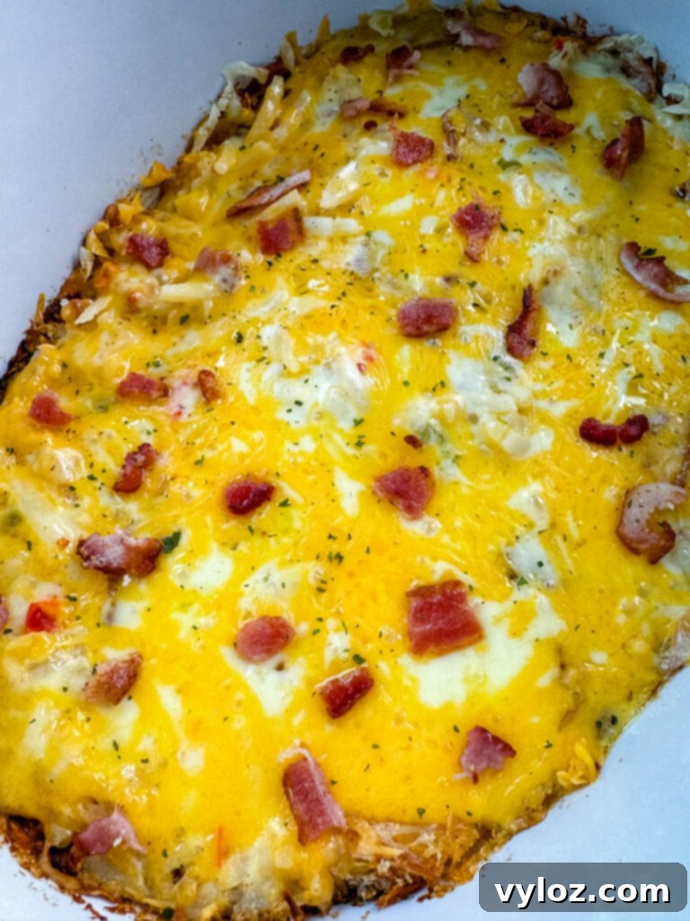 A steaming Crockpot slow cooker filled with golden-brown hash brown casserole, generously topped with melted, bubbly cheese, ready to be served.