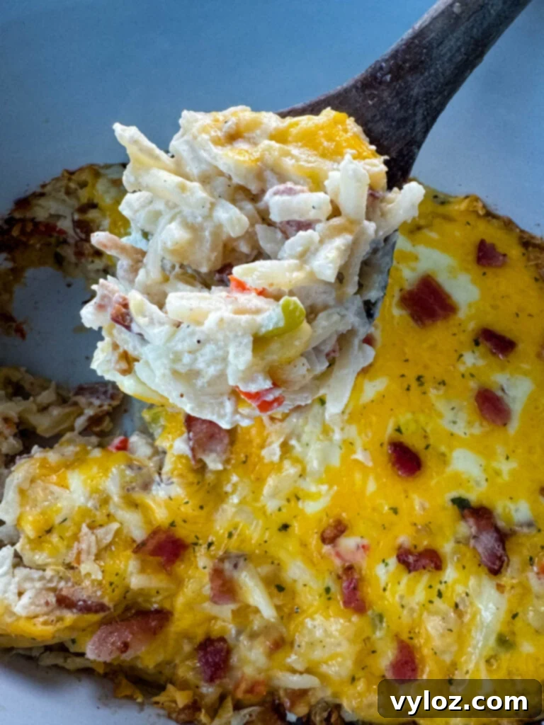 A wooden spoon with a serving of creamy, cheesy hash brown casserole, showing crispy edges and a melted interior, held over a slow cooker.