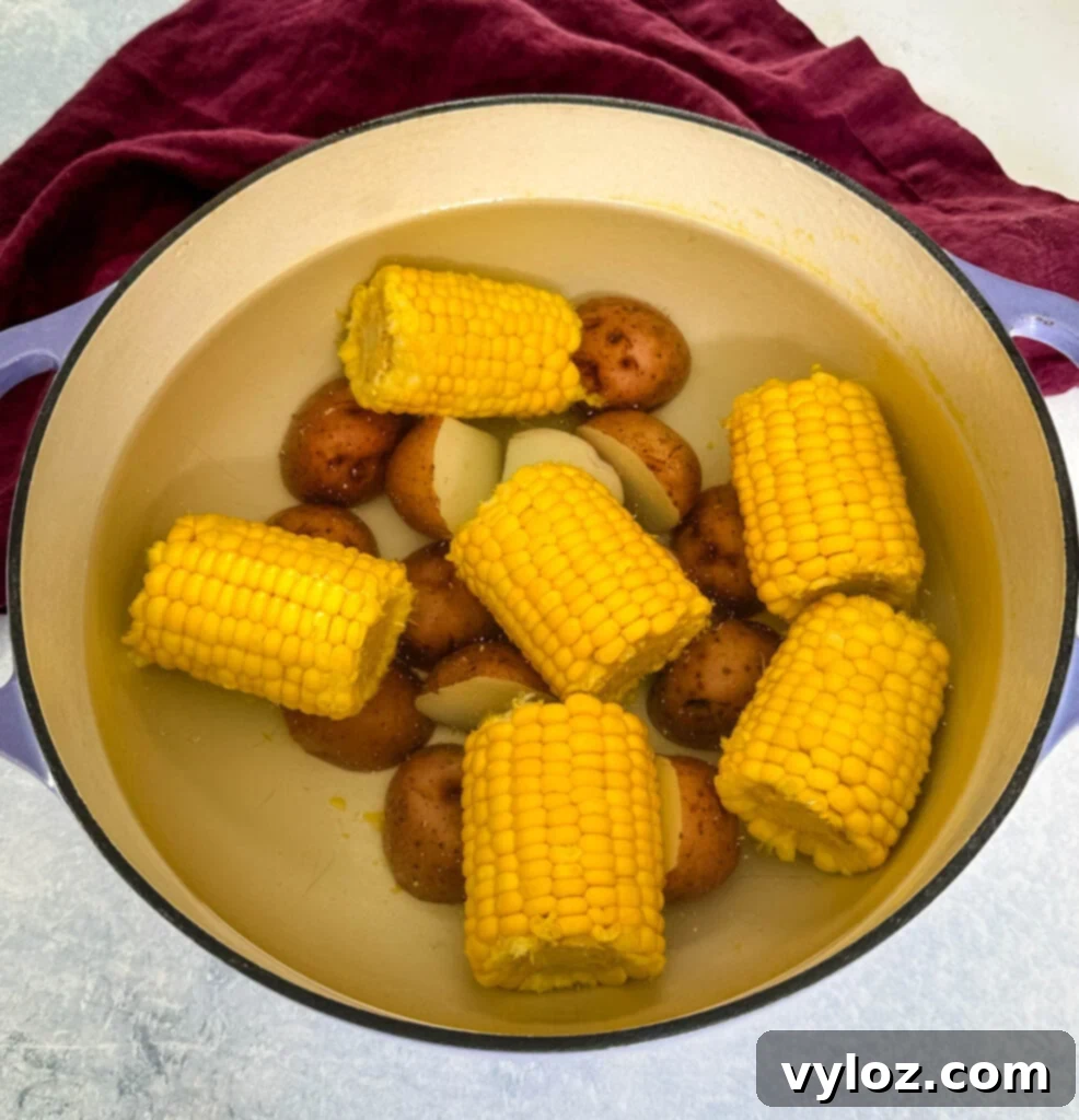 Garlic Butter Seafood Boil Bag 8 Fresh corn on the cob and sliced red potatoes with water in a Dutch oven, illustrating the par-boiling step.