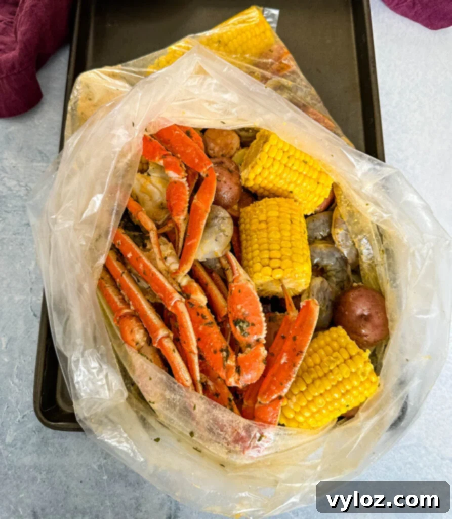 Garlic Butter Seafood Boil Bag 10 A close-up of a cooked seafood boil in a bag, featuring snow crab clusters, shrimp, potatoes, corn on the cob, and sausage.