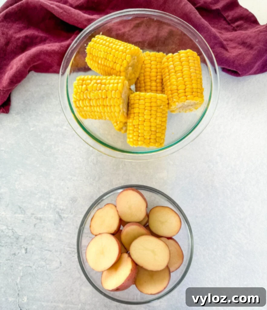 fresh corn on the cob and sliced red potatoes in separate glass bowls