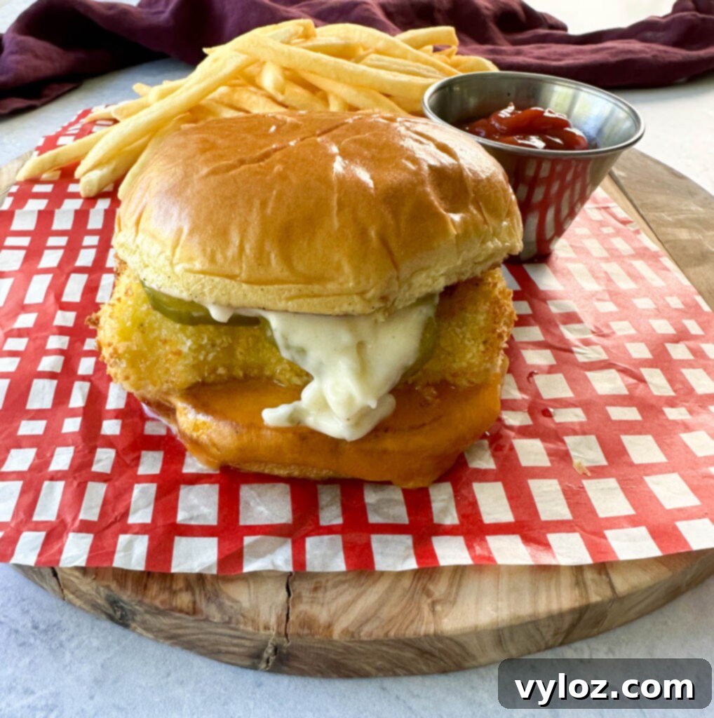 Golden Fried Fish Sandwich 2 fish sandwich with cheese, pickles, and tartar sauce on a brioche bun on a plate with fries