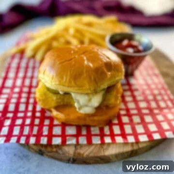 Golden Fried Fish Sandwich 12 fish sandwich with cheese, pickles, and tartar sauce on a brioche bun on a plate with fries