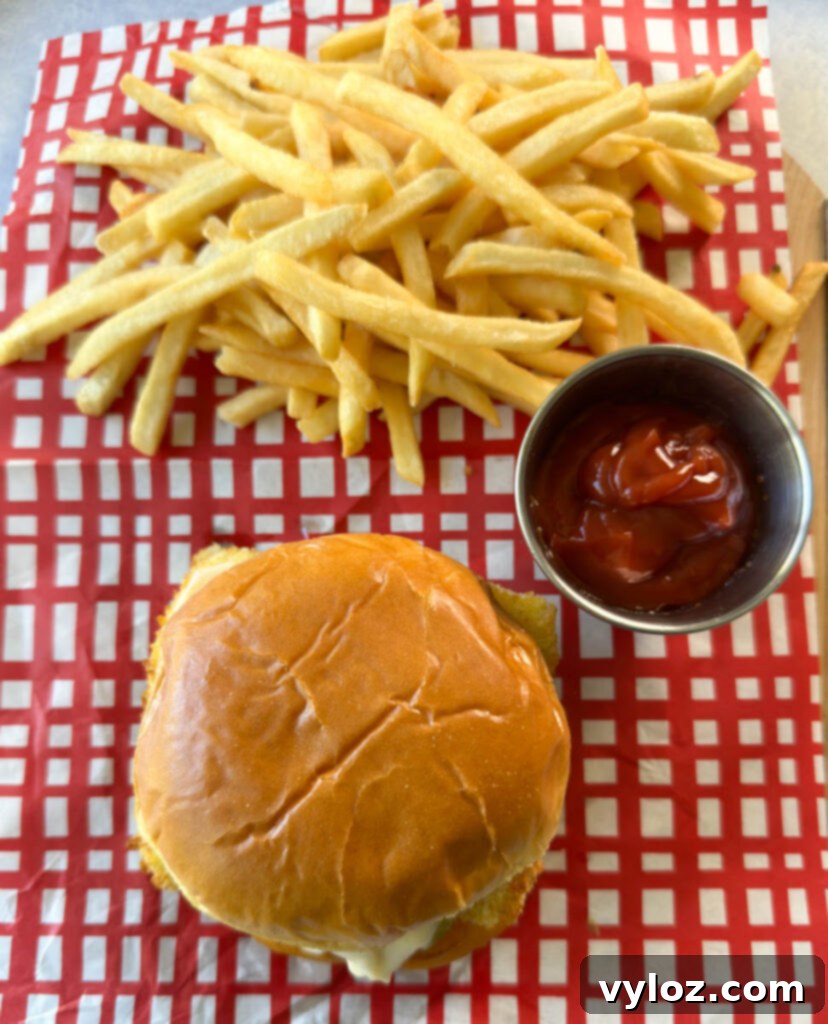 Golden Fried Fish Sandwich 9 fish sandwich with cheese, pickles, and tartar sauce on a brioche bun on a plate with fries