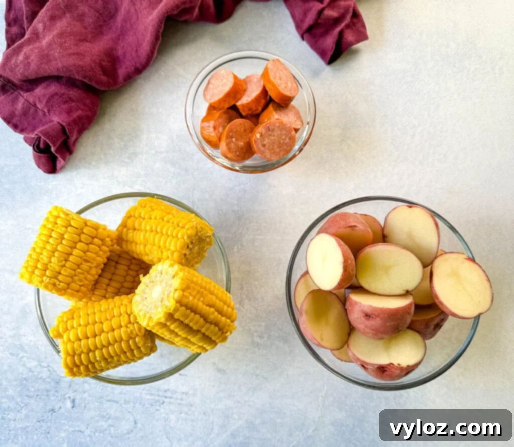 Cajun Crawfish Feast 3 Andouille sausage, corn on the cob, and red potatoes in separate glass bowls, ready for a crawfish boil