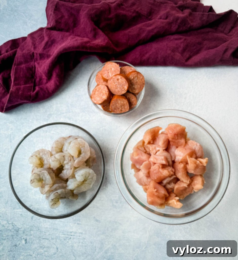 smoked sausage, raw shrimp, and raw chicken thighs in separate glass bowls