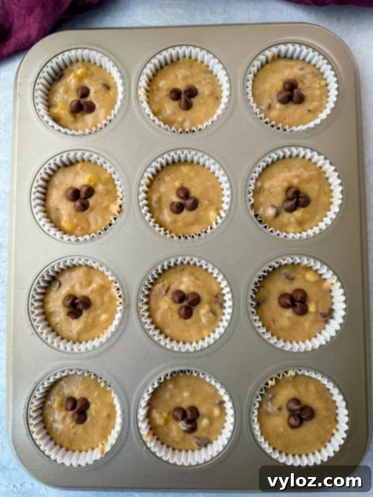 Unbaked banana protein muffin batter with chocolate chips filling a muffin tin, ready for the oven.