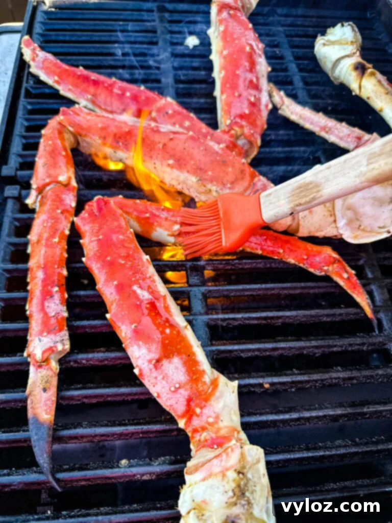 Grilled king crab legs being brushed with garlic butter on a hot grill