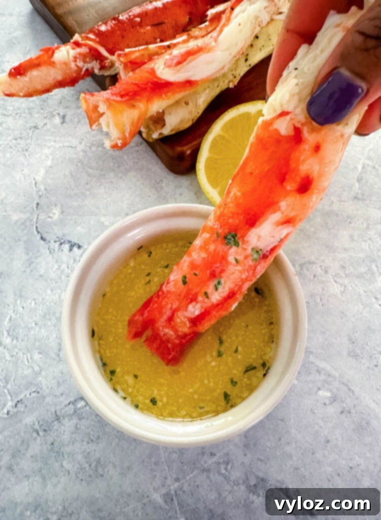 Person holding a cracked king crab leg, dipping it into a bowl of melted garlic butter