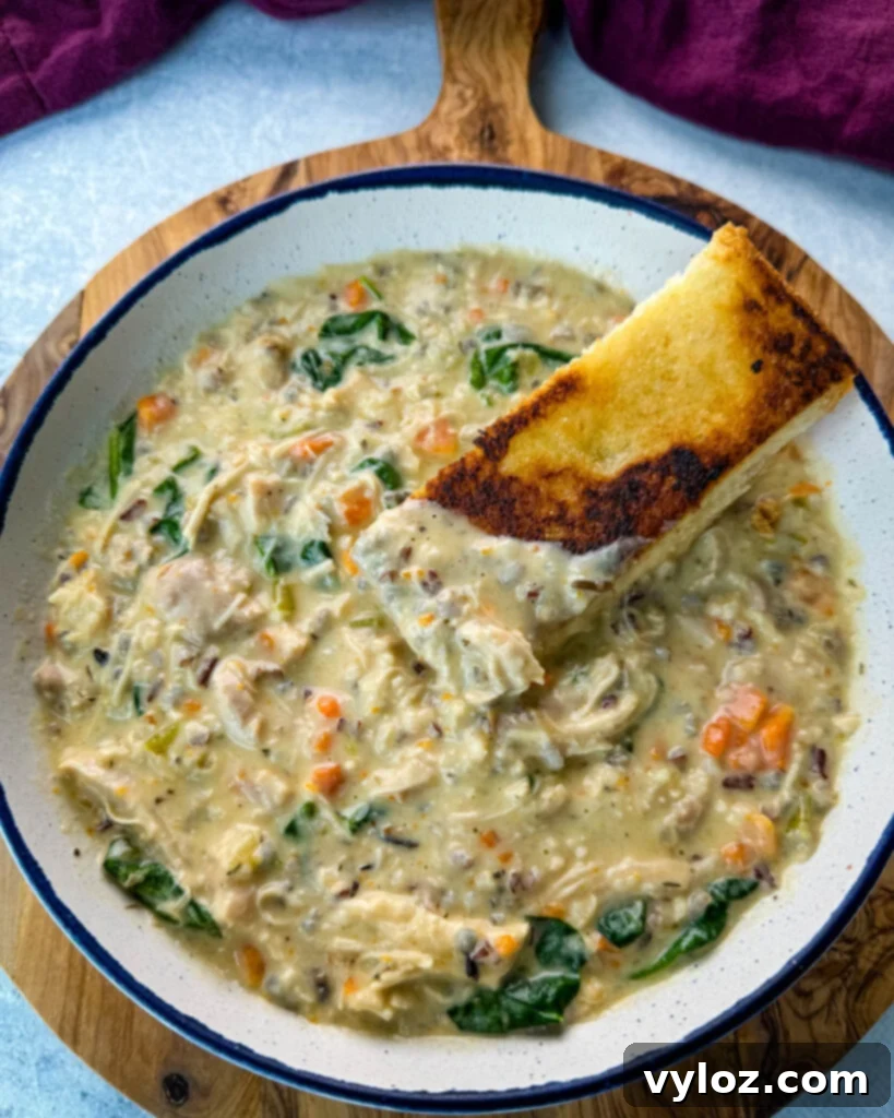 Velvety Chicken Wild Rice Soup 12 Chicken wild rice soup in a white bowl with a slice of toasted bread, ready to be enjoyed.