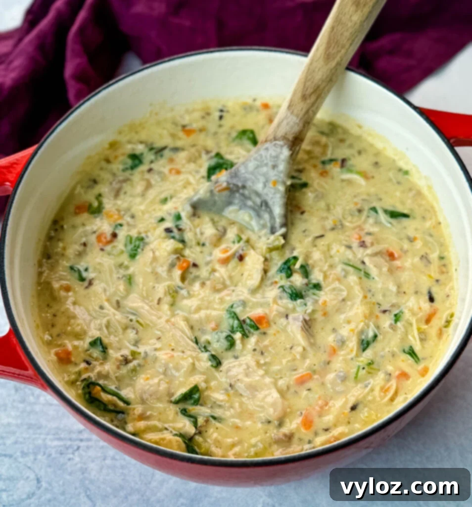 Velvety Chicken Wild Rice Soup 7 Creamy chicken wild rice soup in a red Dutch oven with a wooden spoon, ready to be served.