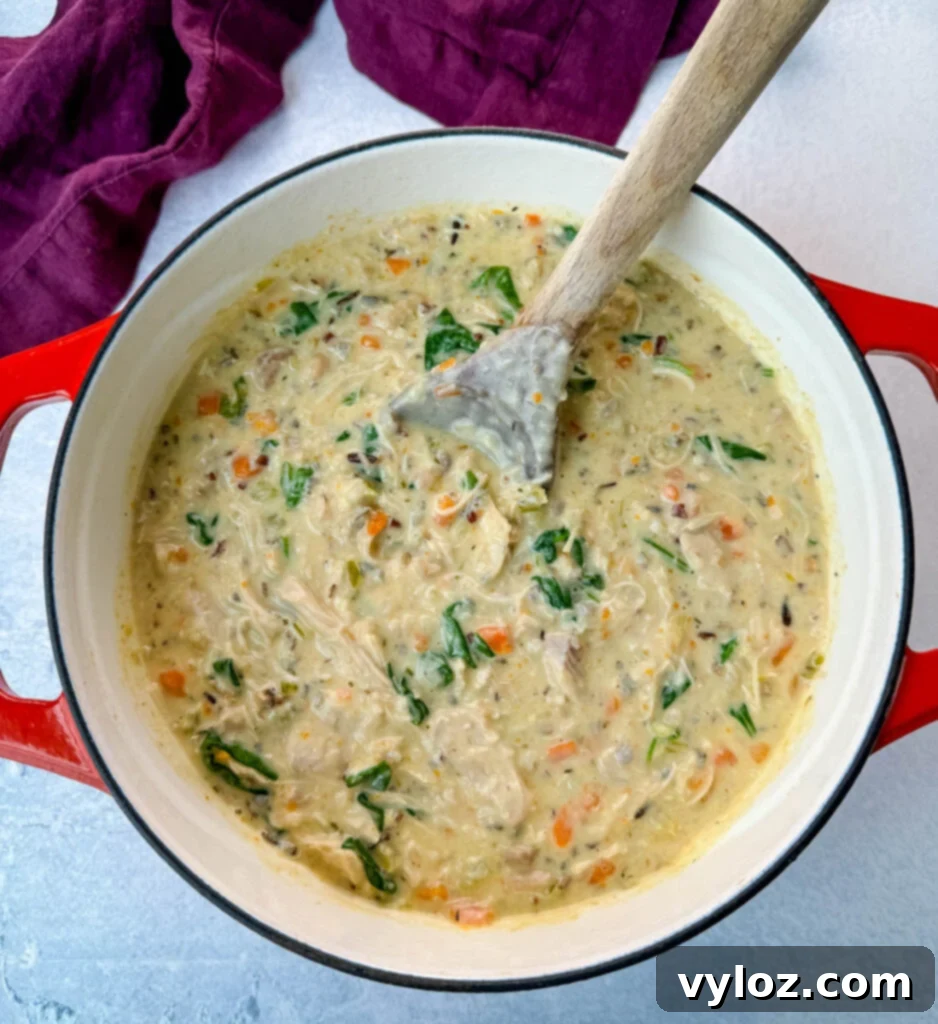 Velvety Chicken Wild Rice Soup 8 Creamy chicken wild rice soup in a red Dutch oven with a wooden spoon, garnished with fresh herbs.