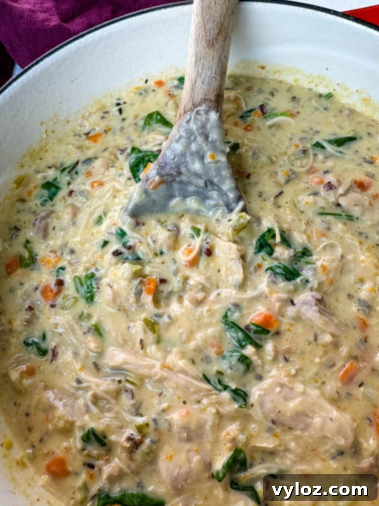 Velvety Chicken Wild Rice Soup 9 Creamy chicken wild rice soup in a red Dutch oven with a wooden spoon, showcasing its thick, rich consistency.
