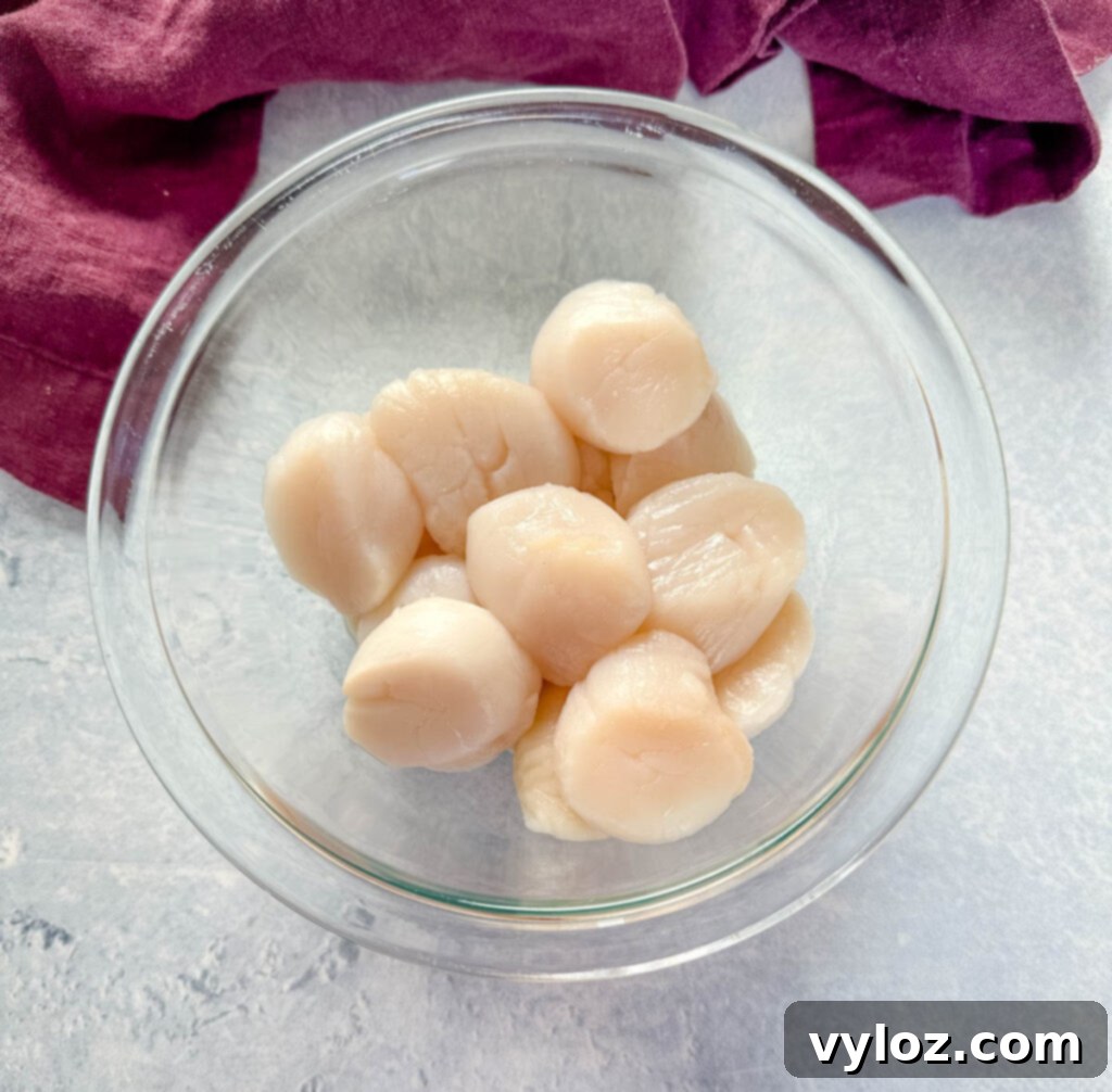 Raw, fresh sea scallops in a clear glass bowl, showcasing their plump texture and natural color.