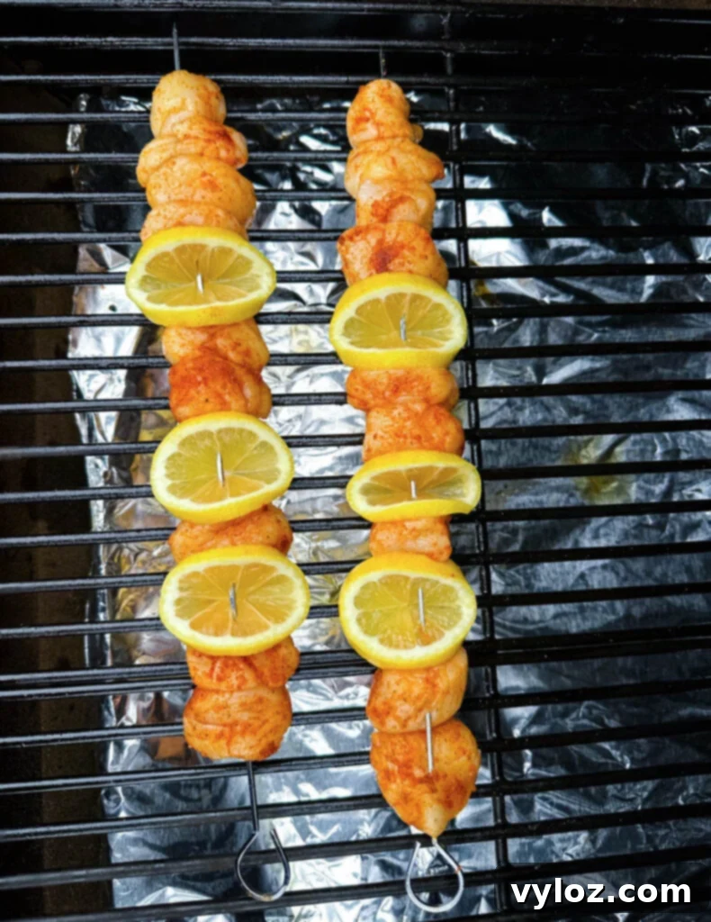 Skewers of scallops and lemon slices smoking on the grates of a Traeger pellet grill, with visible smoke.