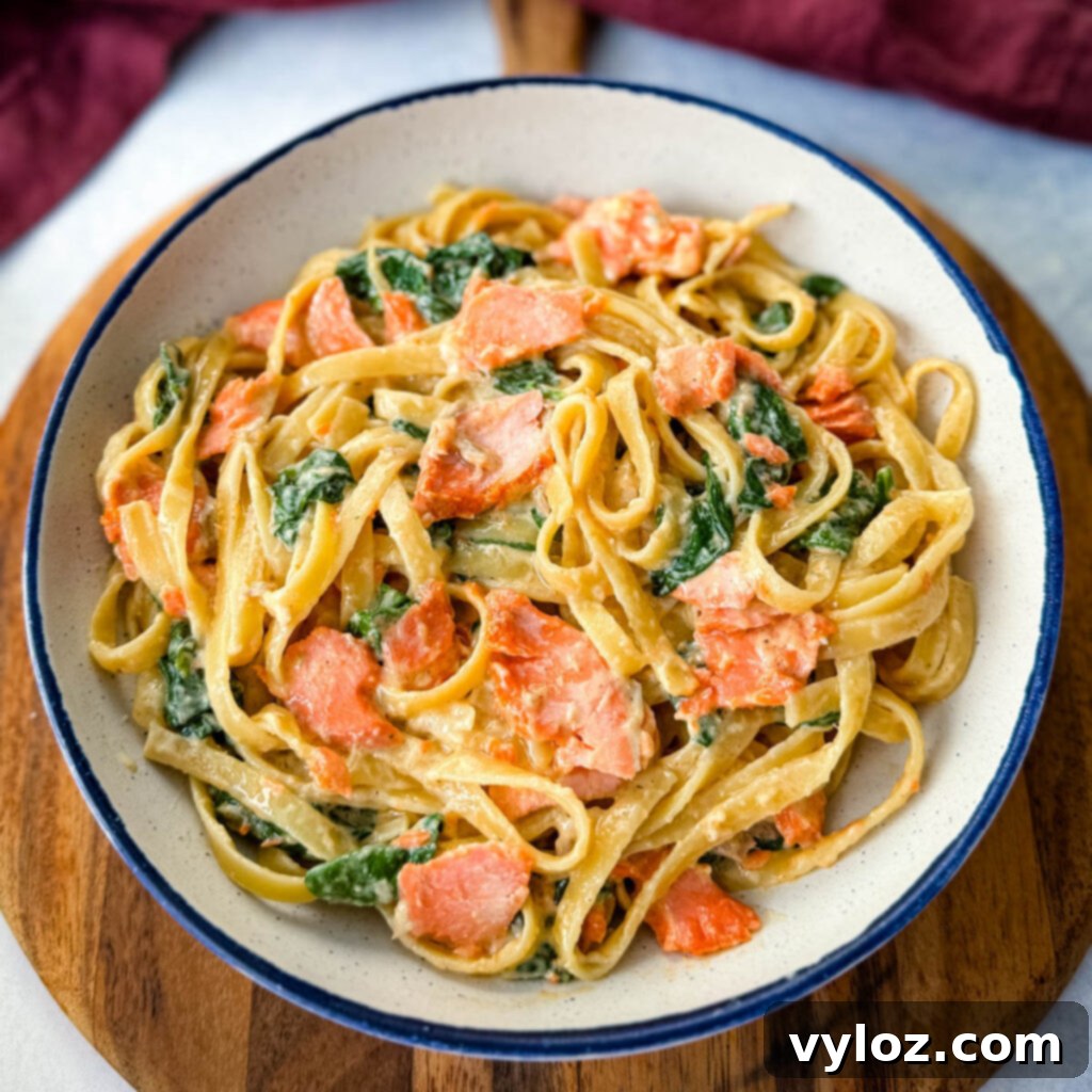 Creamy Salmon Fettuccine Alfredo with fresh spinach served in a white bowl, garnished with herbs.