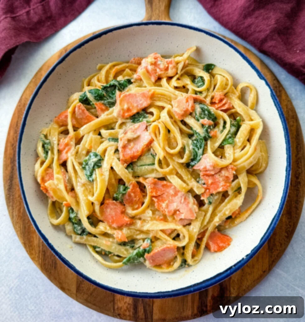 A serving of Salmon Fettuccine Alfredo with spinach in a white bowl, ready to be eaten.