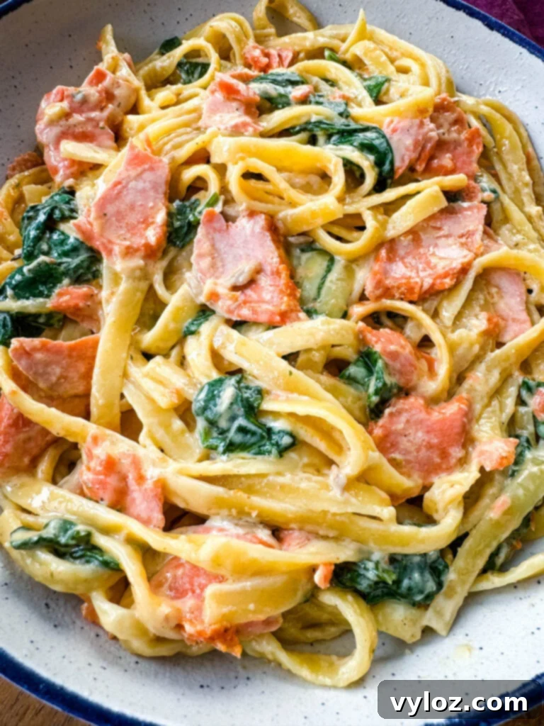 A forkful of creamy Salmon Fettuccine Alfredo with spinach being lifted from a white bowl.