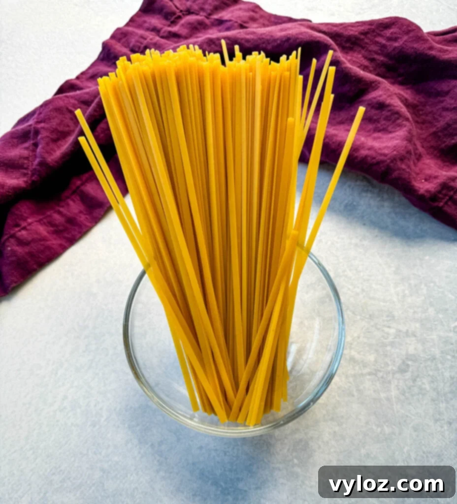 Dry fettuccine pasta arranged in a clear glass bowl, showcasing its flat ribbon shape.
