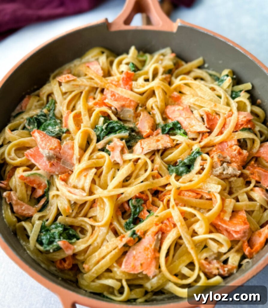 Overhead view of Salmon Fettuccine Alfredo with spinach in a large, deep pan, garnished with fresh herbs.