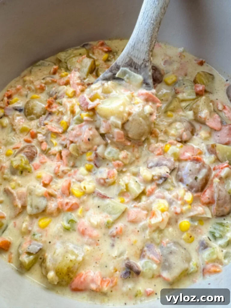 A close-up of creamy salmon chowder with corn and potatoes in a Dutch oven, garnished with fresh dill.