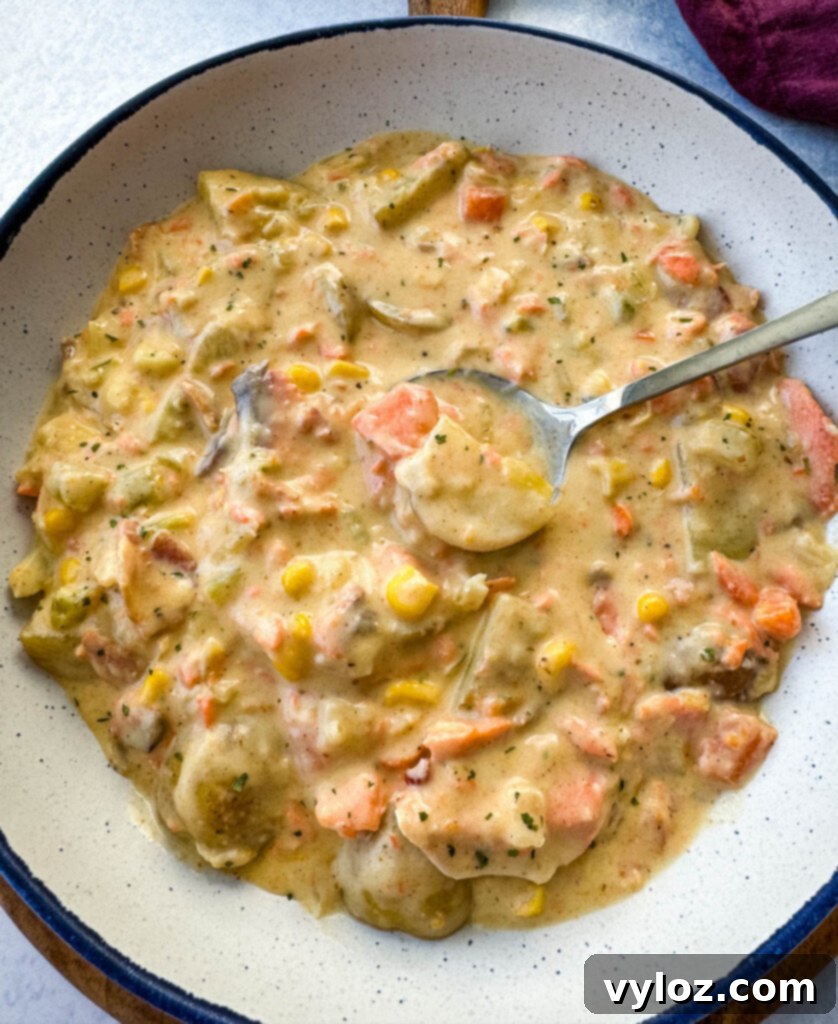 A serving of creamy salmon chowder with corn and potatoes in a white bowl with a spoon, ready to eat.