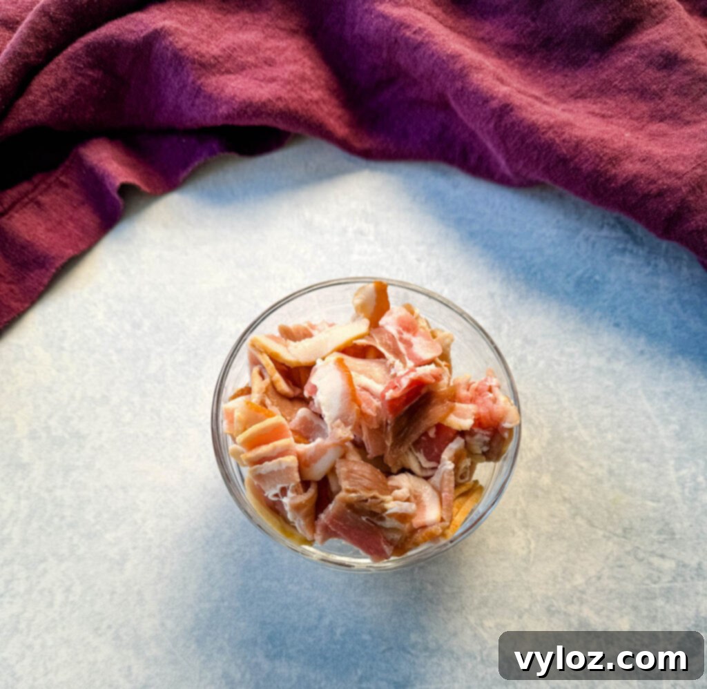 Uncooked bacon slices neatly arranged in a clear glass bowl, ready for chopping.