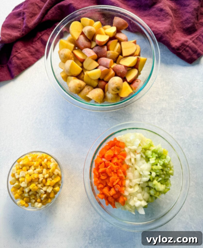 A collection of raw vegetables including potatoes, corn, carrots, celery, and onions in separate glass bowls.