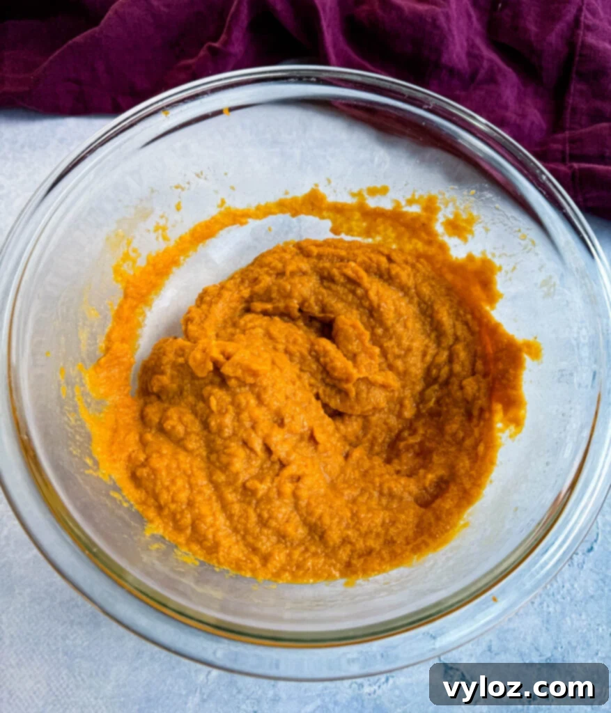 A glass bowl filled with vibrant orange pureed pumpkin, ready to be incorporated into the muffin batter.