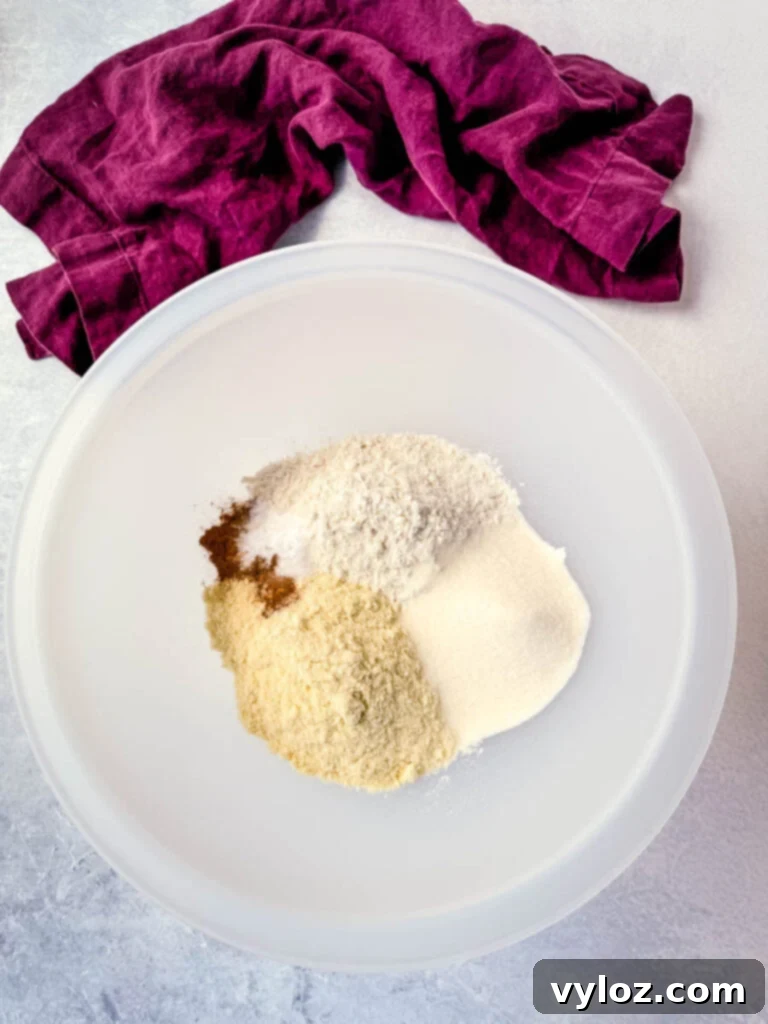 A large mixing bowl containing a dry mix of protein powder, all-purpose flour, pumpkin pie spice, sweetener, and baking soda, ready for the wet ingredients.