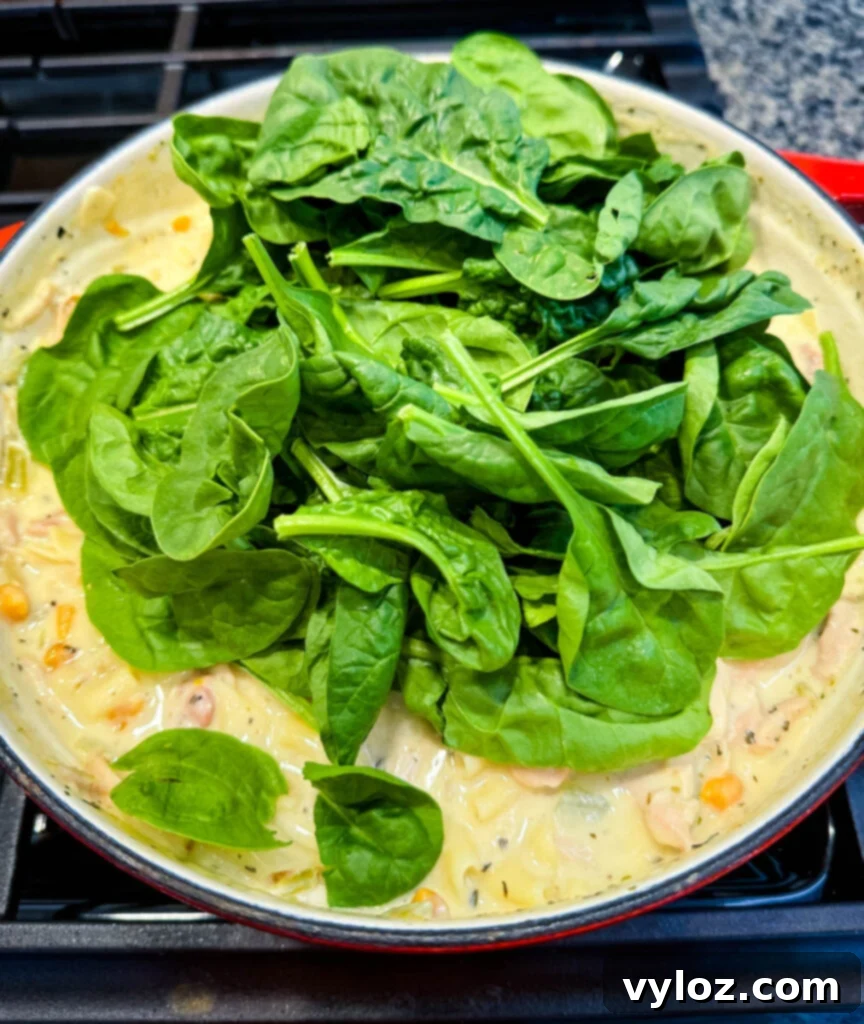 Creamy White Lasagna Soup 11 White Lasagna Soup in a Dutch oven with fresh spinach wilting into the hot broth.