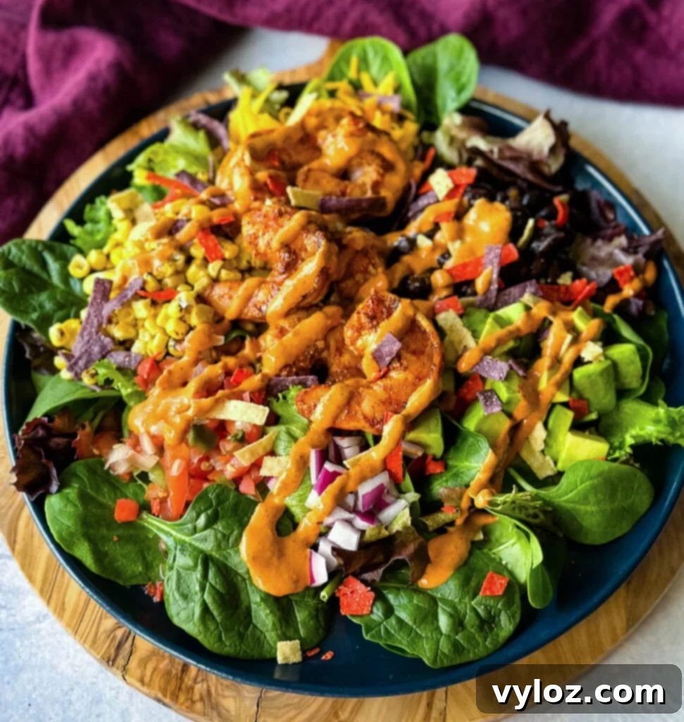 Zesty Shrimp Taco Bowl 2 A vibrant shrimp taco salad featuring avocado, corn, black beans, red onions, and a generous drizzle of Chipotle ranch dressing, served on a striking blue plate.